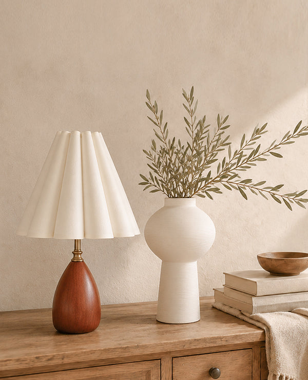 A table lamp, ceramic vase, books, and textiles arranged in a warm interior.